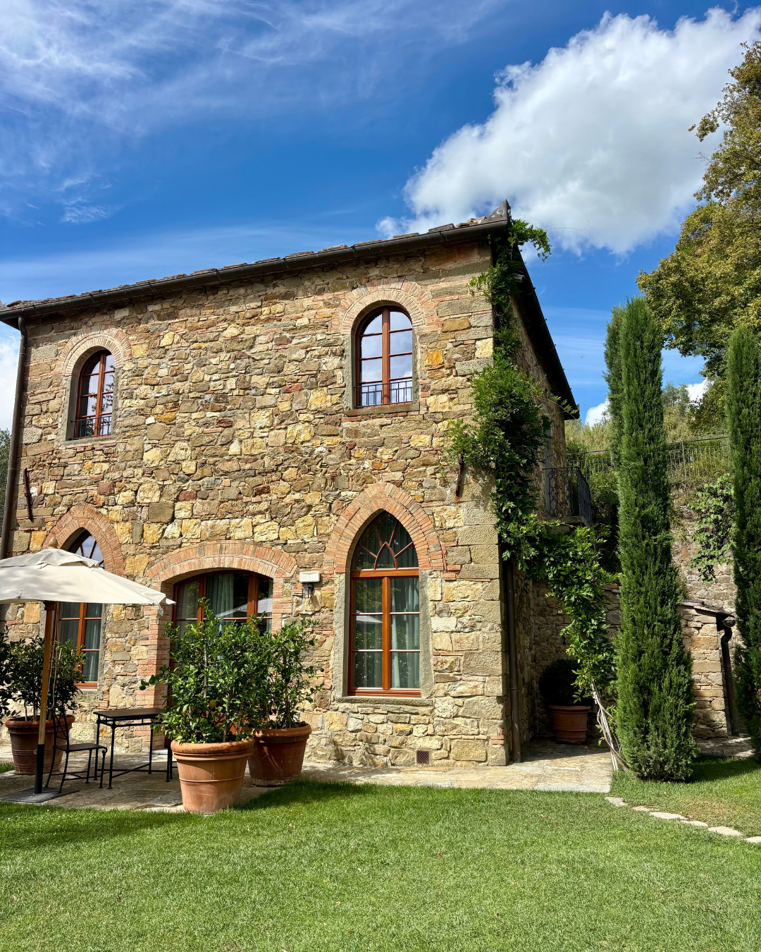 Stone country house framed by lawn and cypress trees