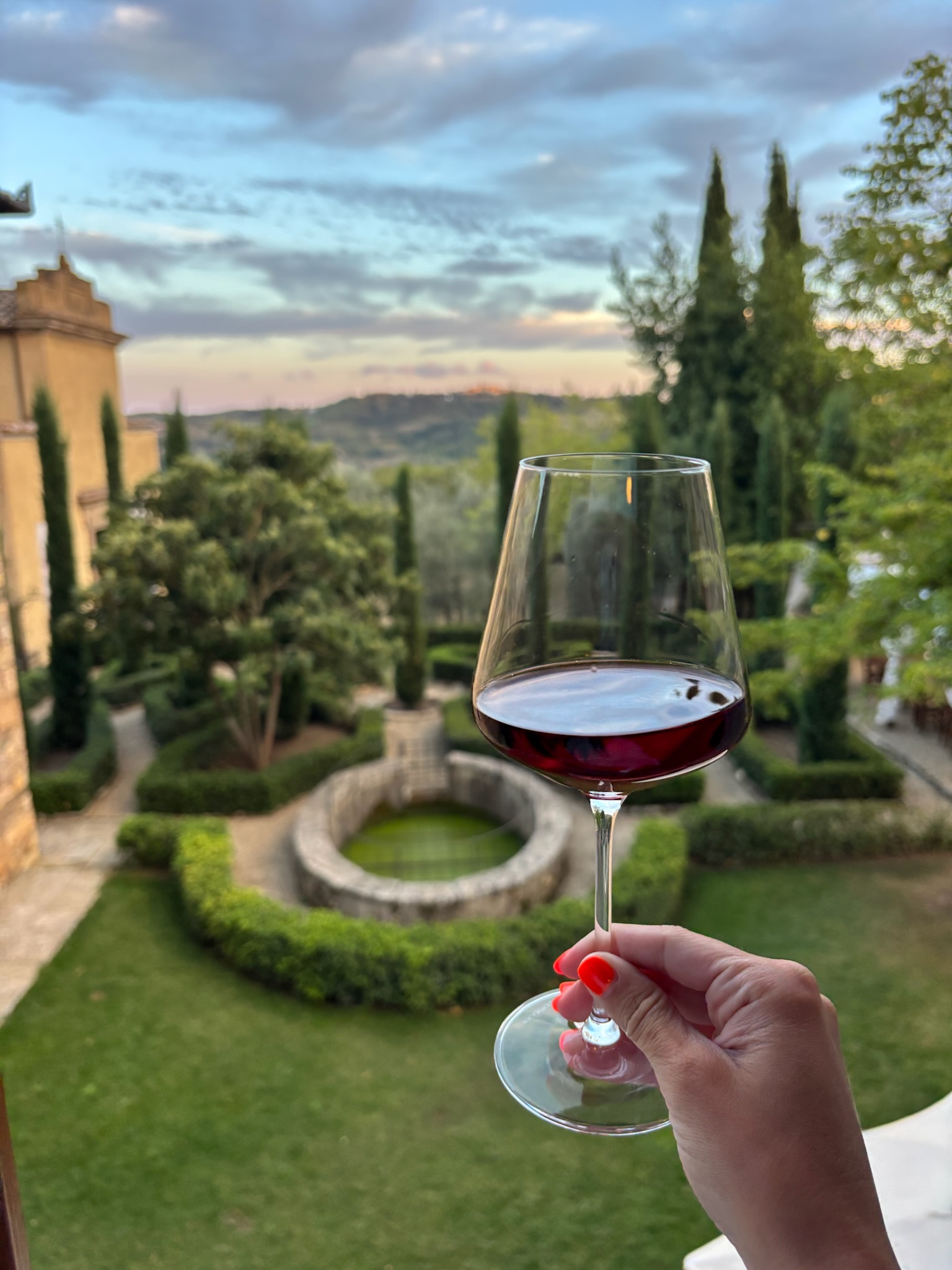 A glass of red wine overlooking a formal Tuscan garden and countryside